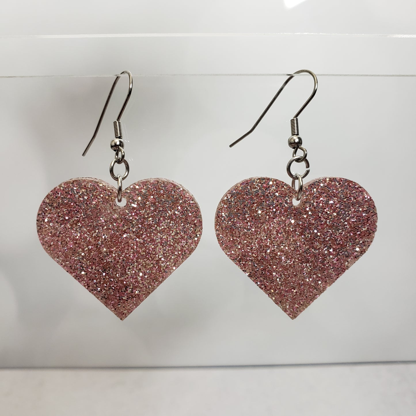 Rose gold tone glitter acrylic heart shaped dangle earrings hanging on display for reference.