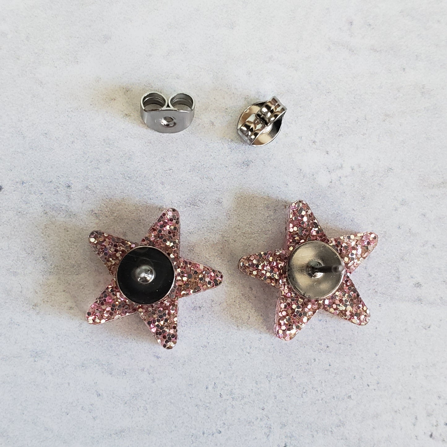 Backside of rose gold tone glitter star stud earrings showing posts