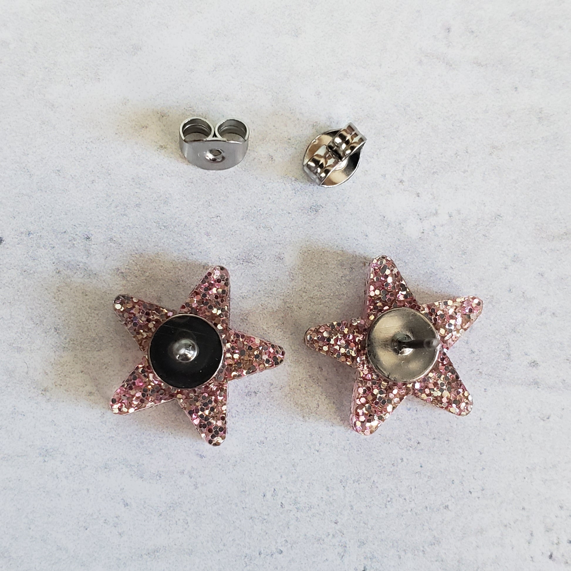 Backside of rose gold tone glitter star stud earrings showing posts