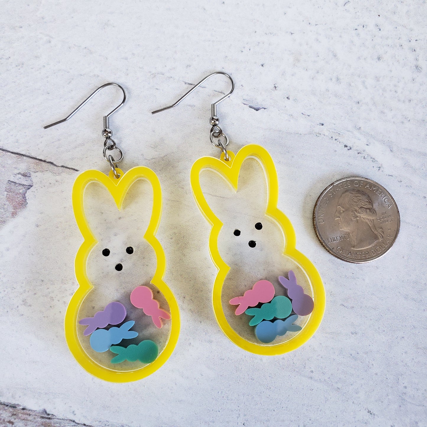 Marshmallow bunny shaker earrings in yellow with pastel bunnies inside on stainless steel earring wires next to quarter for size.