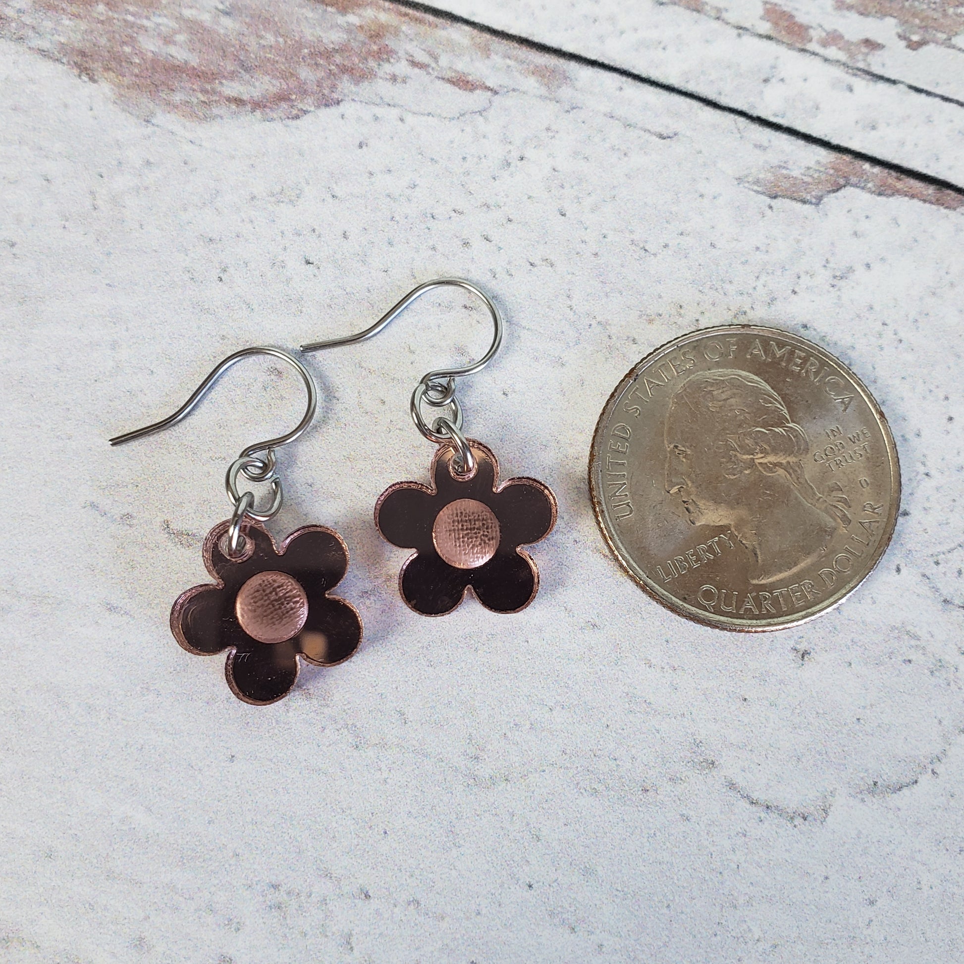 Rose gold mirror daisy earrings on stainless steel earring wires next to quarter for size reference.