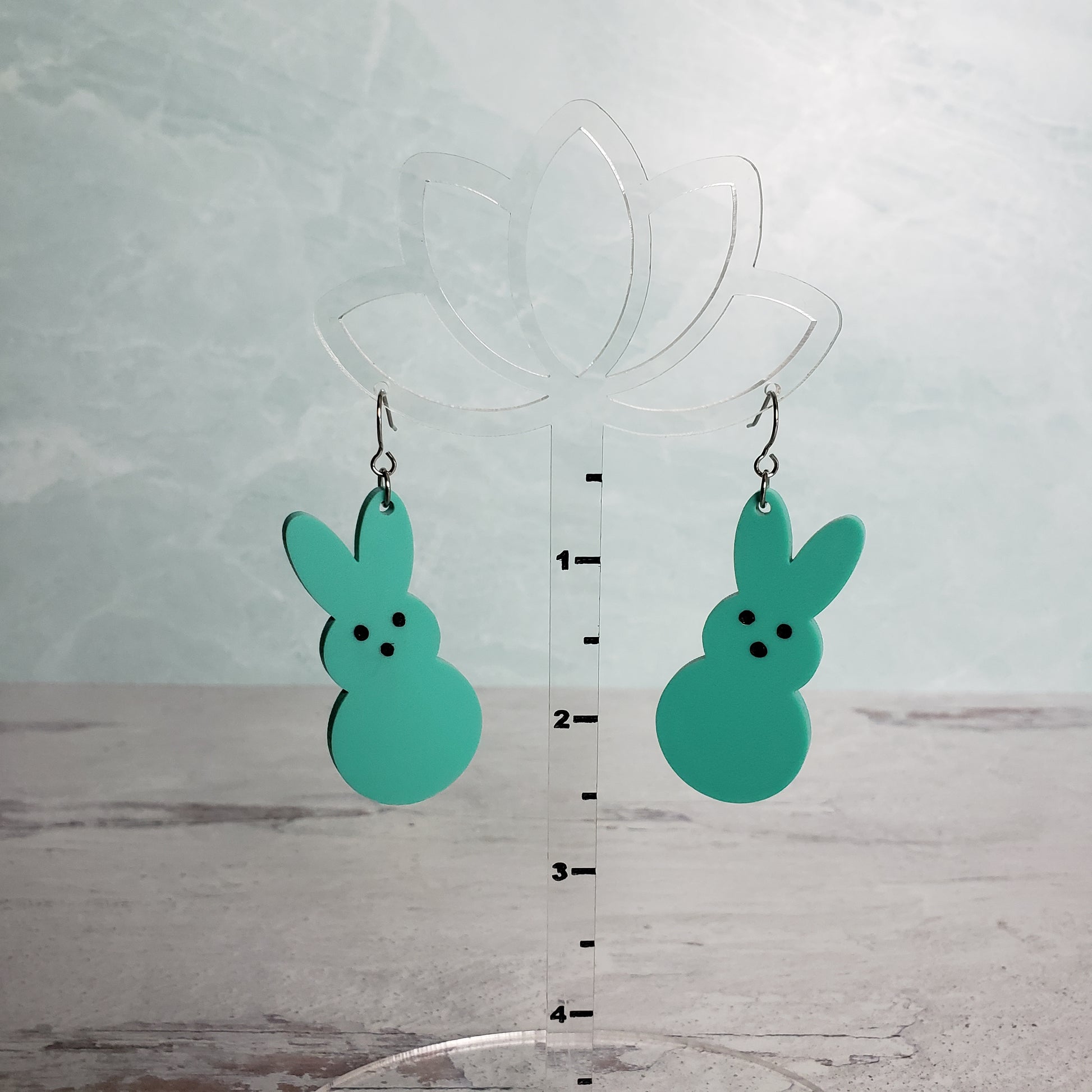Matte Mint Green Marshmallow Bunny Earrings on stainless earring wires on hanging display for size.