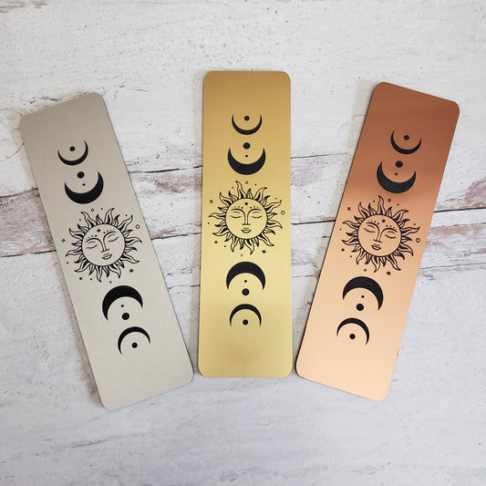3 Celestial themed moon phase bookmarks with sun in center.  Shows from left to right as silver tone, gold tone, and rose gold tone.
