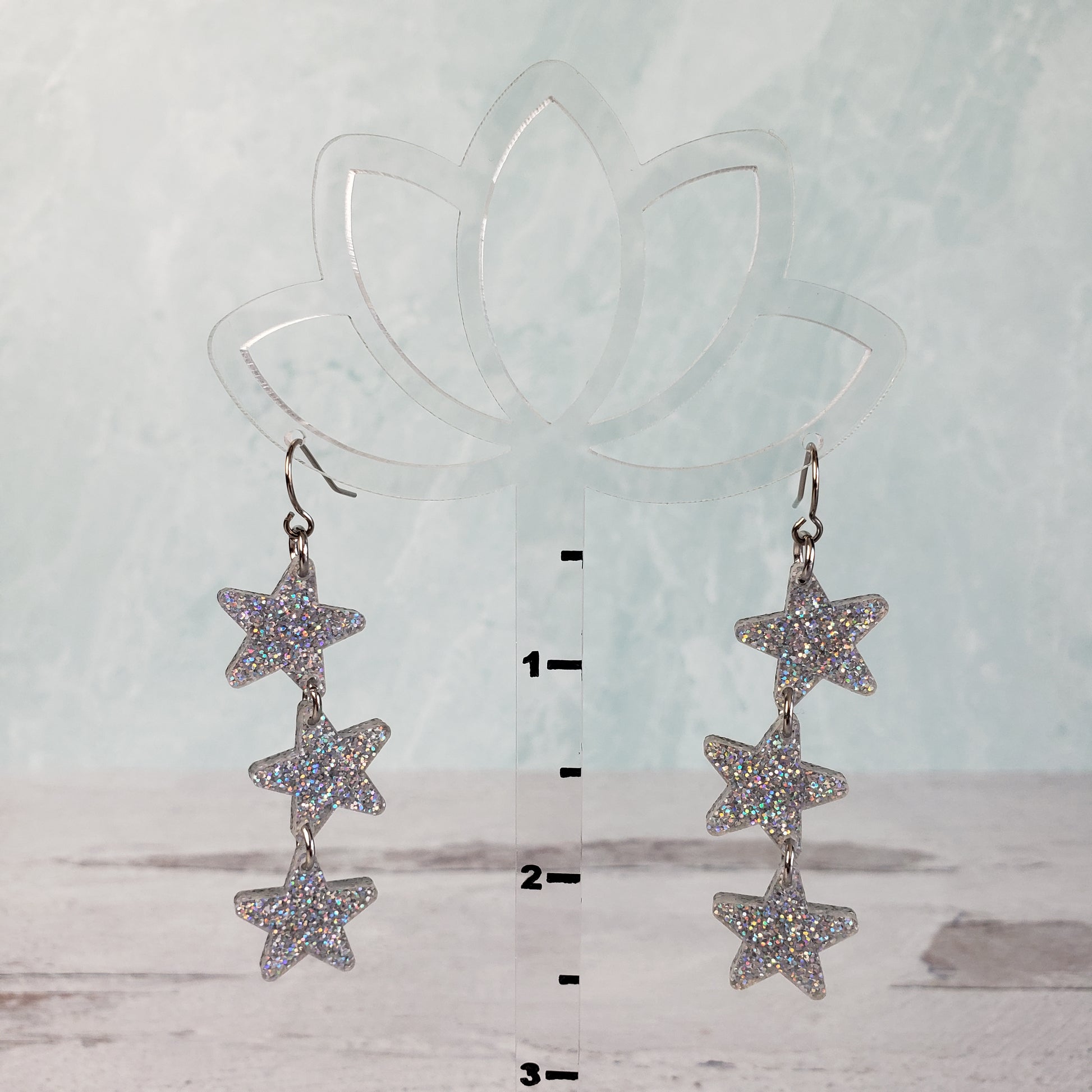 Silver holographic star dangle earrings on hanging display for size reference