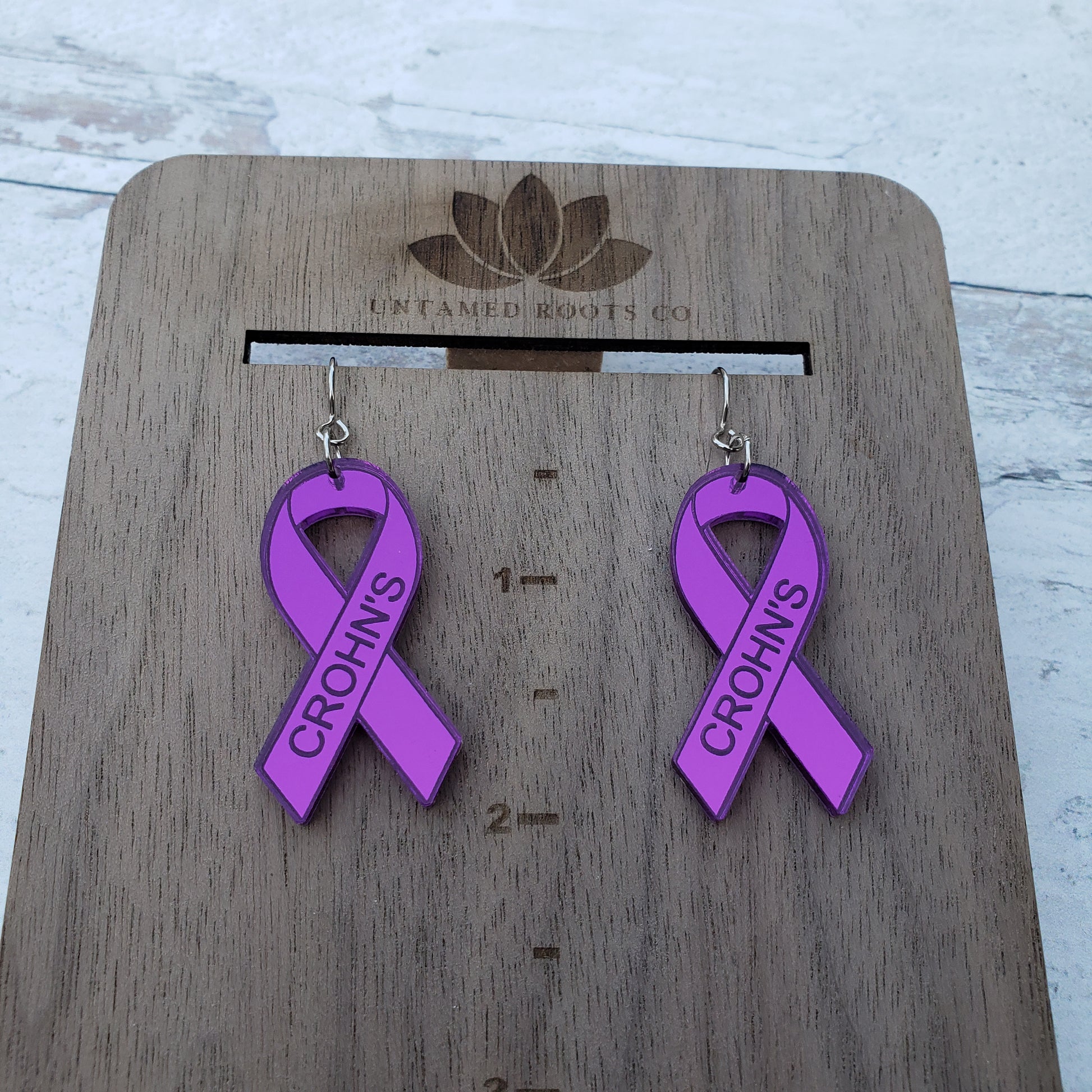 Crohn's Engraved purple mirror acrylic awareness ribbons on stainless steel earring wires. On hanging display for size.