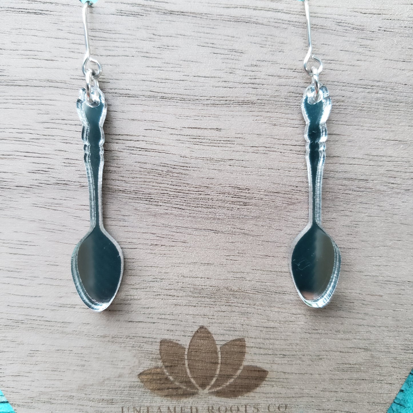 Close up image of silver mirror spoon shaped dangle earrings on stainless steel earring wires