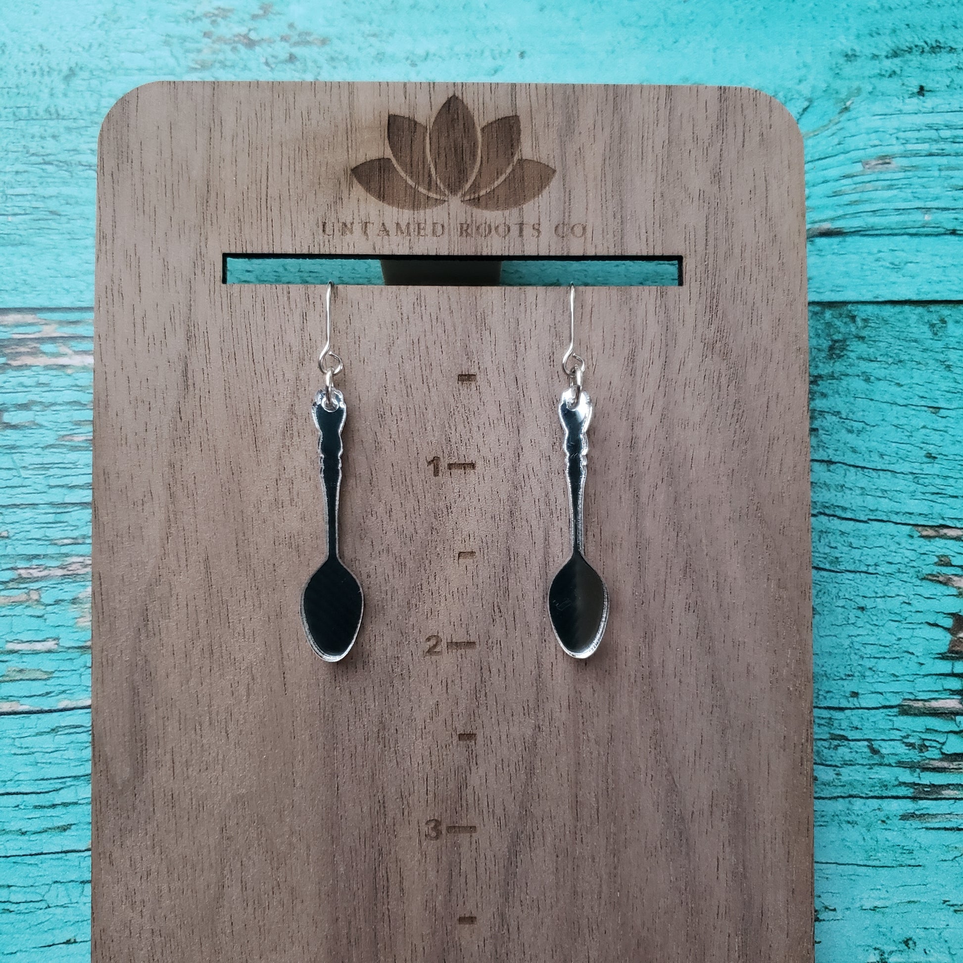 Silver spoon shaped earrings on stainless steel earring wires on hanging measuring display