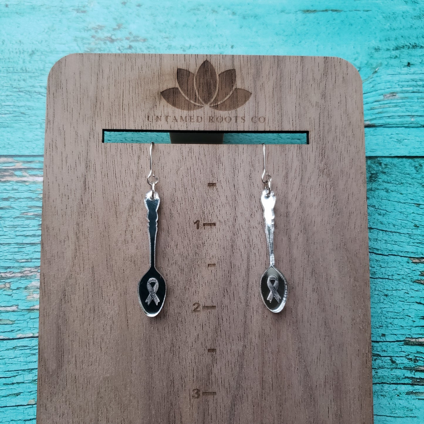 Silver mirror spoon shaped dangle earrings on wooden hanging display for size reference.