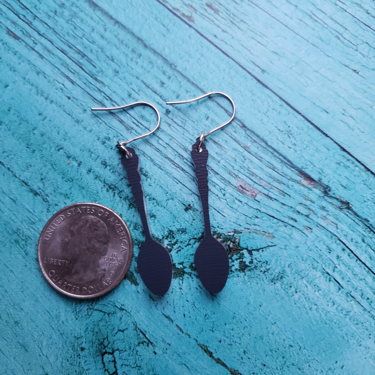 Backside of silver spoon earrings next to quarter for size.