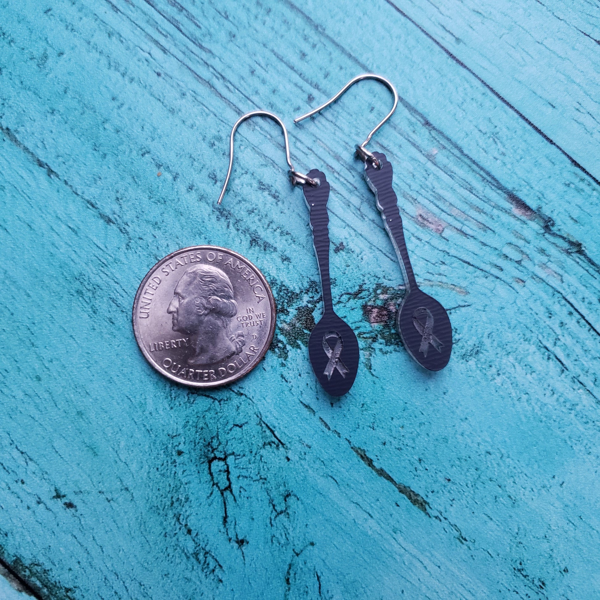 Backside of ribbon engraved silver spoon earrings next to quarter for size reference.
